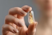 Glowing golden DNA helix molecule inside transparent capsule held between fingers against blurred background, representing genetic medicine and biotechnology research.