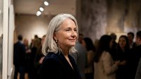 Senior woman with gray hair smiling at art gallery opening event with blurred crowd in background, cultural lifestyle and social gathering concept.