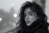Young Hispanic woman with tousled dark hair wearing black scarf looking away thoughtfully against blurred city lights background in dramatic black and white portrait.