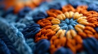Vibrant orange and navy blue crochet flower pattern in extreme macro photography showing detailed yarn texture and intricate stitch work with selective focus effect.