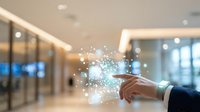 Young male professional with medium skin tone in business attire touching digital network interface with glowing particles and light effects in modern office environment for technology and innovation concepts.