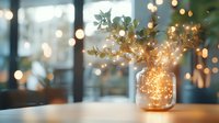 Magical glowing fairy lights in glass jar with eucalyptus branches create cozy atmosphere against blurred bokeh background, perfect for holiday decor and celebrations.
