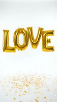 Gold foil letter balloons spelling LOVE floating above scattered heart confetti on white background, perfect for Valentine's Day and wedding celebrations.