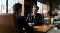 Professional mature Caucasian businesswoman in gray suit conducting job interview with male candidate in modern corporate office with city view.