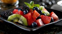 Fresh fruit salad with watermelon, kiwi, blackberries and blueberries garnished with mint leaves served in black ceramic plate on dark background.