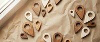 Wooden location pin icons scattered on craft paper background. GPS navigation symbols for mapping apps, travel websites, and location-based services design.