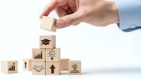 Hand placing wooden cube with business icons forming pyramid structure representing growth strategy and development planning for corporate success.