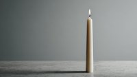 Single beige candle with flame on wooden surface against gray wall background for home decor and relaxation concepts.