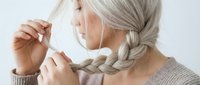 Senior woman with long gray braided hair adjusting protective face mask, healthcare and safety concept for medical and wellness campaigns.