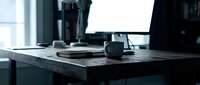 Minimalist workspace with dark desk, coffee mug, notebook, and computer monitor in modern office environment for professional productivity and creative work.