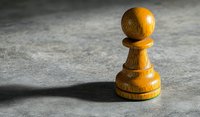 Wooden chess pawn piece casting dramatic shadow on concrete surface, symbolizing strategy and leadership in business and competition.