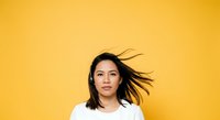 Young Asian woman with shoulder-length black hair wearing white t-shirt against bright yellow background, hair in motion, suitable for lifestyle and portrait photography.