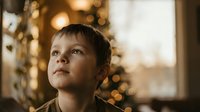 Young boy gazing upward with wonder during golden hour, warm bokeh lights creating magical atmosphere for holiday storytelling and childhood dreams.