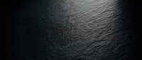 Dark textured surface with dramatic lighting creating subtle shadows and depth, suitable for backgrounds, overlays, and design projects.