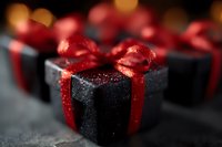Black gift box with sparkling glitter texture and red satin ribbon bow on dark background with bokeh lights, macro close-up shot for holiday season.