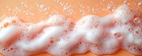 White soap foam and bubbles on peach or coral colored background, macro photography showing texture and detail of cleaning product lather.