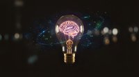 Glowing light bulb with pink brain inside against dark background with bokeh lights representing creativity, innovation, intelligence and bright ideas concept.