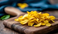 Fresh raw pasta sheets piled on rustic wooden cutting board, bright yellow homemade Italian noodles against dark wood background, selective focus for culinary use.