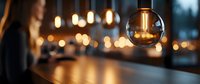 Glowing vintage Edison bulb pendant lamp against blurred warm bokeh background creates cozy atmospheric lighting in modern interior space.