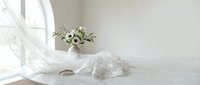 Minimalist white bedroom interior with flowing curtains, fresh flowers in vase and rumpled bedding creating serene morning atmosphere for home decor concepts.