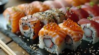 Fresh sushi rolls with salmon, tuna and red caviar served on black slate plate. Traditional Japanese cuisine with rice, nori and sesame seeds.