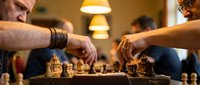 Two focused men playing strategic chess game in warm indoor setting with soft lighting and concentrated atmosphere.