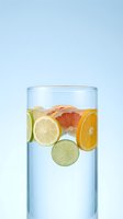 Fresh citrus fruit slices floating in clear glass of water on light blue background for healthy lifestyle and detox concepts.