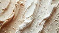 Creamy beige foundation makeup texture with smooth swirls and droplets on white background for cosmetic and beauty product advertising campaigns.