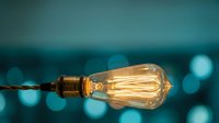 Vintage Edison bulb glowing with warm filament against blurred teal bokeh background creating atmospheric lighting for modern interior design concepts.