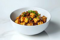 Crispy mapo tofu with minced meat and Sichuan peppercorns garnished with fresh green onions served in white ceramic bowl on marble surface.
