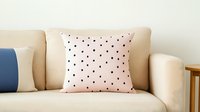 Pink throw pillow with navy polka dots pattern on beige couch, modern minimalist home decor accent piece for living room or bedroom interior styling.