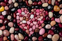 Heart shape made of pink and red pebbles surrounded by natural stones in various colors and sizes on dark background, romantic nature composition.