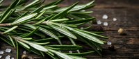 Fresh rosemary sprigs with sea salt crystals and peppercorns on dark wooden surface for culinary and cooking projects.