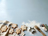 Overhead view of star-shaped cookies dusted with powdered sugar, wooden utensils, and fresh rosemary on light blue surface. Baking and holiday cooking.