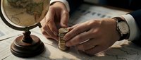 Businessman hands stacking coins on desk with globe and documents. Financial planning, investment strategy, global business growth concept.