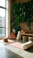 Modern urban jungle living room with lush green plants against exposed brick wall, natural light streaming through large windows creating serene indoor garden atmosphere.