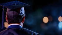Rear view of male graduate in cap and gown against dark background with bokeh lights, symbolizing achievement and future opportunities.
