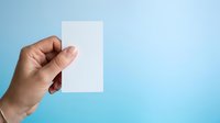 Close-up of a hand holding a blank white card against a blue background, suitable for business presentations, marketing mockups, and advertising campaigns.
