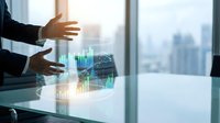 Businessman in dark suit analyzing holographic financial data charts and graphs on glass surface with city skyline background for business analytics and investment concepts.