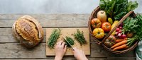 Fresh organic vegetables and herbs on rustic wooden table with hands preparing healthy ingredients for cooking and meal preparation.