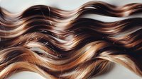 Luxurious wavy brown hair with blonde highlights flowing in soft curves, showcasing natural shine and healthy texture for beauty and haircare advertising.