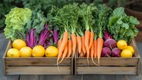 Fresh organic produce in wooden crates including vibrant carrots, beets, lemons, lettuce and leafy greens arranged for farmers market or healthy food display.