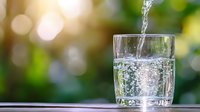 Fresh sparkling water being poured into clear glass with bubbles against blurred green nature background for healthy hydration lifestyle.