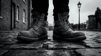 Worn leather boots standing on wet urban pavement with city street and lamp post in background, conveying resilience and street style for fashion and lifestyle content.