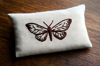 Brown butterfly embroidered on natural linen cushion against wooden surface, showcasing delicate needlework detail and textural contrast. Suitable for craft and decor.