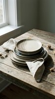 Stacked ceramic plates with linen napkins on rustic wooden table by window, neutral tones, minimalist tableware styling for home decor and dining concepts.