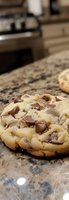 Fresh baked chocolate chip cookie on marble counter, showing gooey melted chips and soft dough texture in close-up macro photography.
