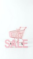 Pink miniature shopping cart placed on sale letters against white background, retail discount and e-commerce promotion concept.