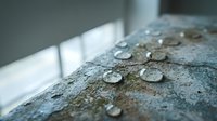 Water droplets on concrete surface with natural window light creating peaceful minimalist composition for wellness and nature concepts.