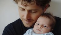 Tender moment between young Caucasian father and newborn baby in soft natural light. Close-up portrait showing emotional connection and paternal love.